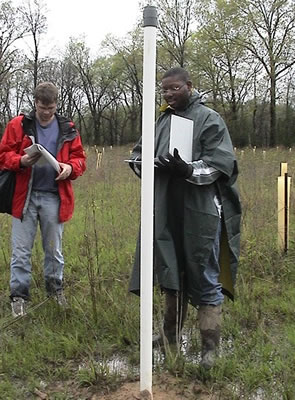 see caption. 2 people standing in marshy area consulting notes and looking at barologger