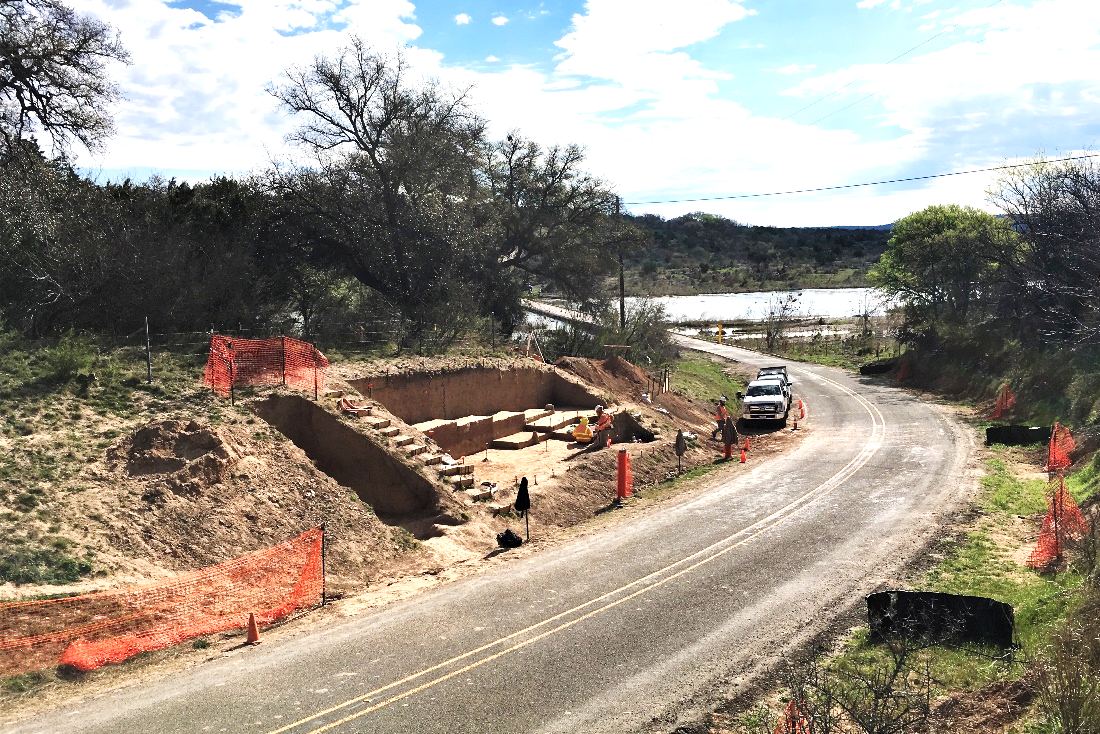 An archeological excavation site on the side of the road with people working in the site.