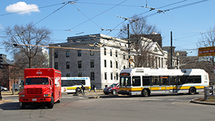 A street with a red truck and two buses entering a roundabout
