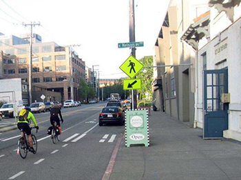 Photograph of two bicyclists traveling along a designated bike lane on a city street near a marked pedestrian crosswalk