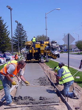 Photograph of a construction crew laying and leveling the concrete of a new sidewalk