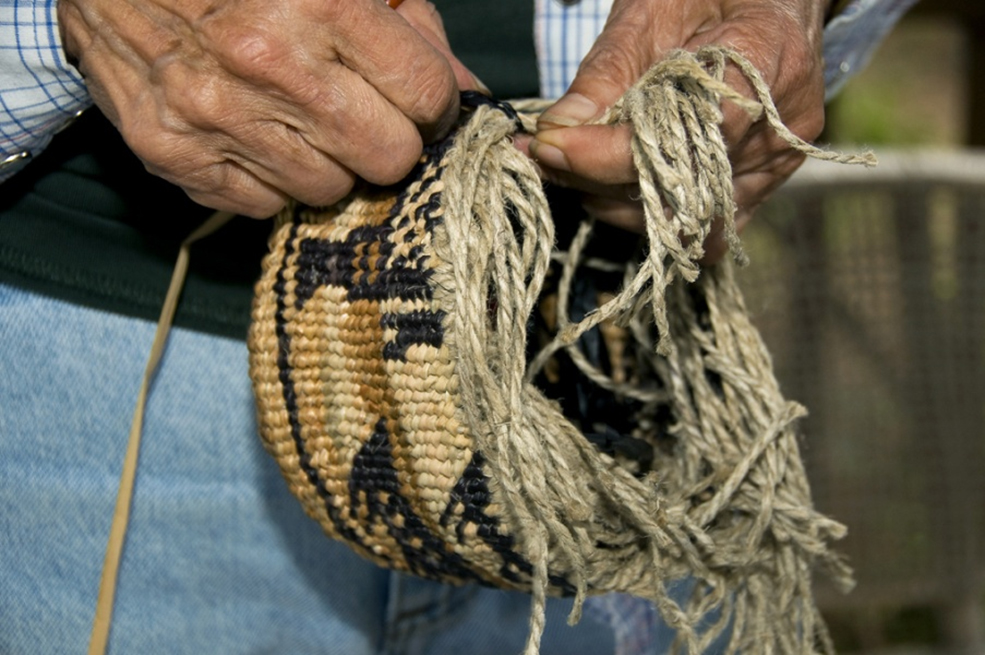 Close up photograph of a Siletz tribe member weaving dogbane fibers into a partially-completed basket