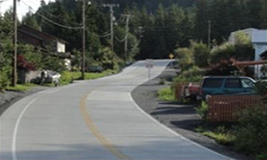 Photograph of the roadway after completion of the Shtax'Heen Roadway Improvement Project, which shows a widened roadway, fresh pavement, clearly marked lanes, and buffer areas on both sides