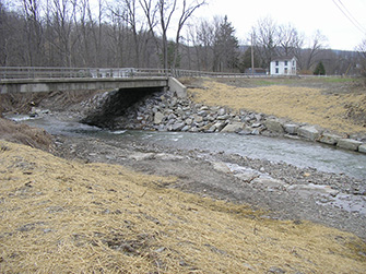 Photograph of the State Route 34 bridge over Cayuga Inlet after riverbank restoration, showing large rocks reinforcing the riverbank