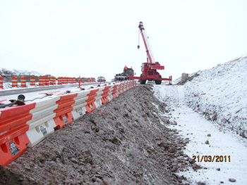 Photograph of the wildlife crossing construction showing orange and white interlocking jersey barriers along the road and a large crane in the distance