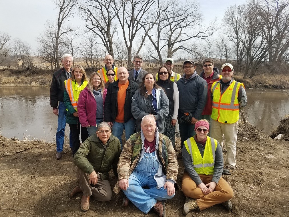 A group of people tribe memebers pose for a picture in front of a river.