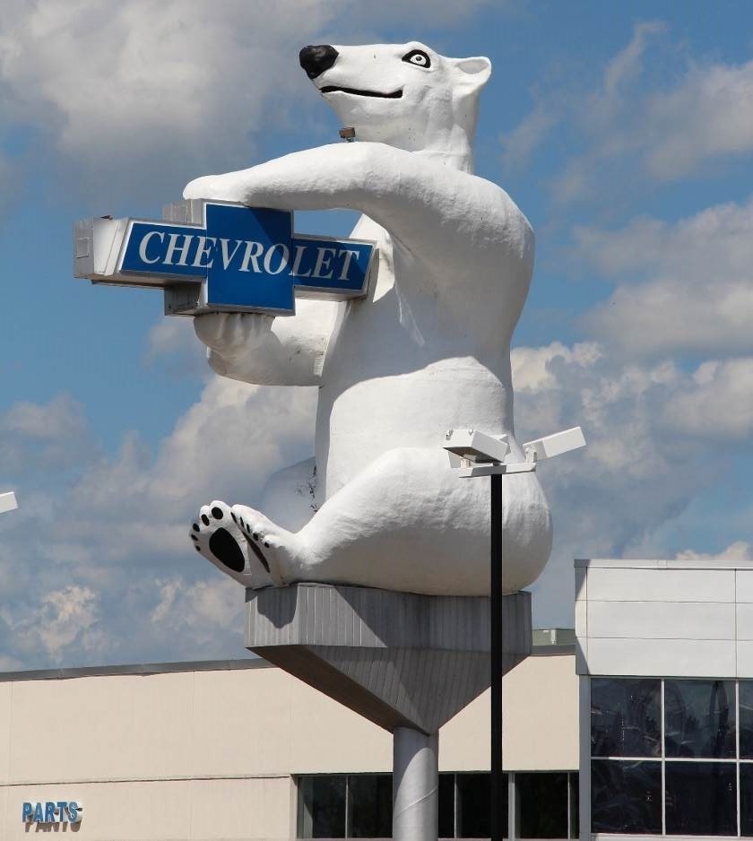A giant three dimensional polar bear holding a Chevrolet sign outside of a car dealership.
