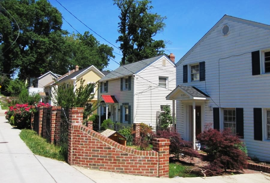 A row of houses on a street with a sidewalk in front of the homes.