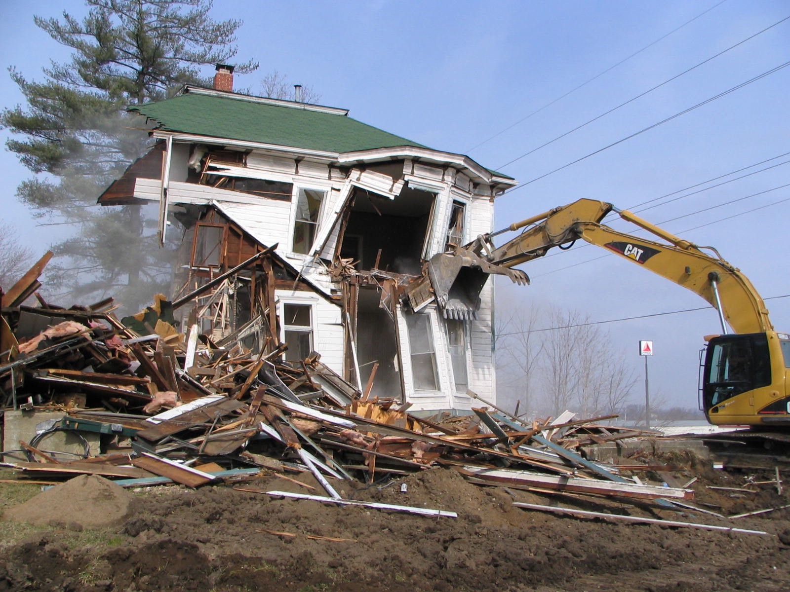 A photograph of a house being torn down by an excavator.