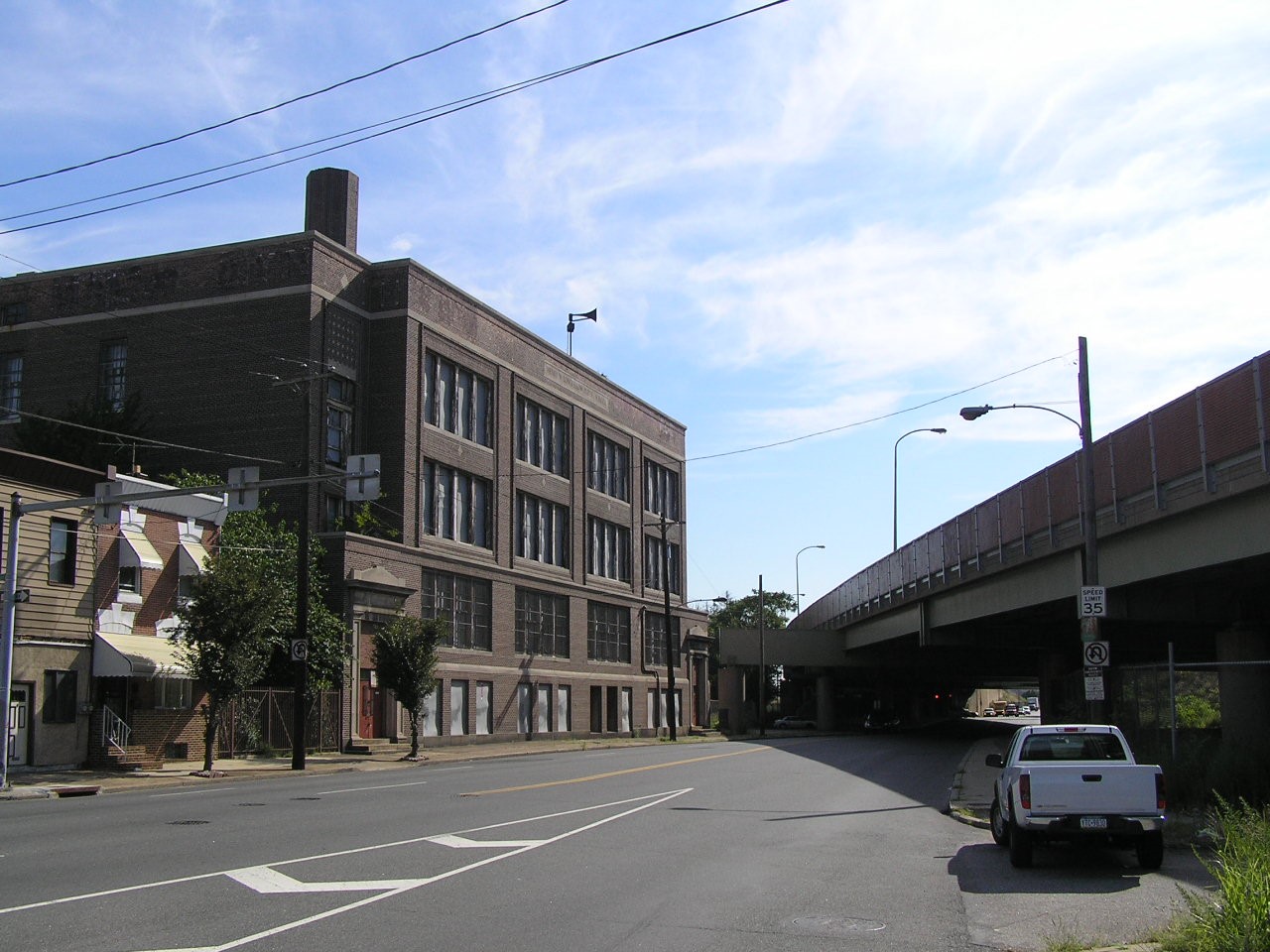 A photograph of a street view with a multi-story brick building right next to an elevated highway.