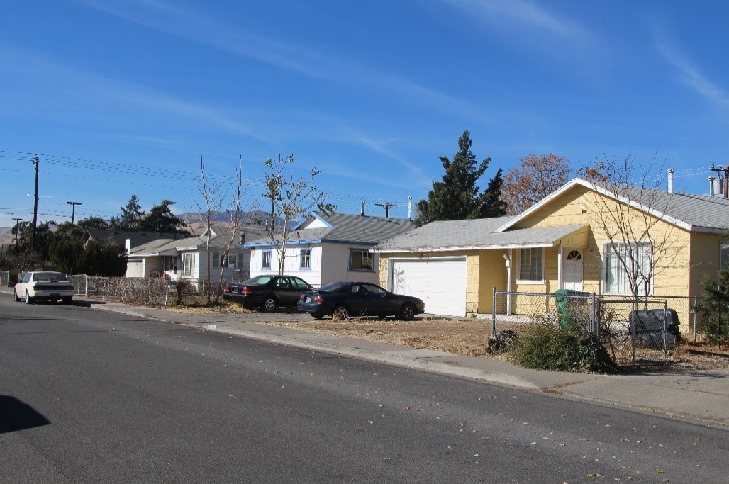 A photograph of a streetscape with three houses lining the street.