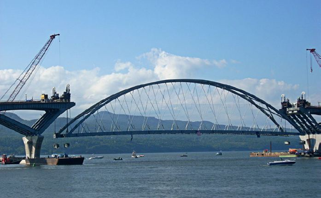 Photograph of Lake Champlain Bridge’s 402-foot arch being lifted from the river into place by cranes